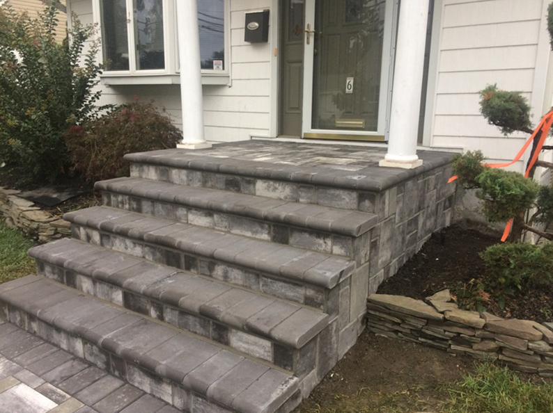 Stone steps leading up to a house's front door; steps, porch, and walls are gray.