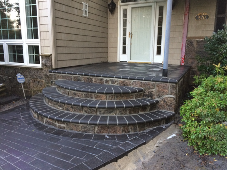 Curved brick steps leading to a house entryway, dark bricks and stone accents.