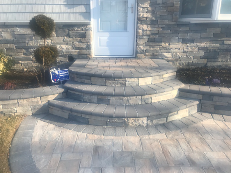 Stone steps leading to a white door, surrounded by stone walls and a brick walkway.