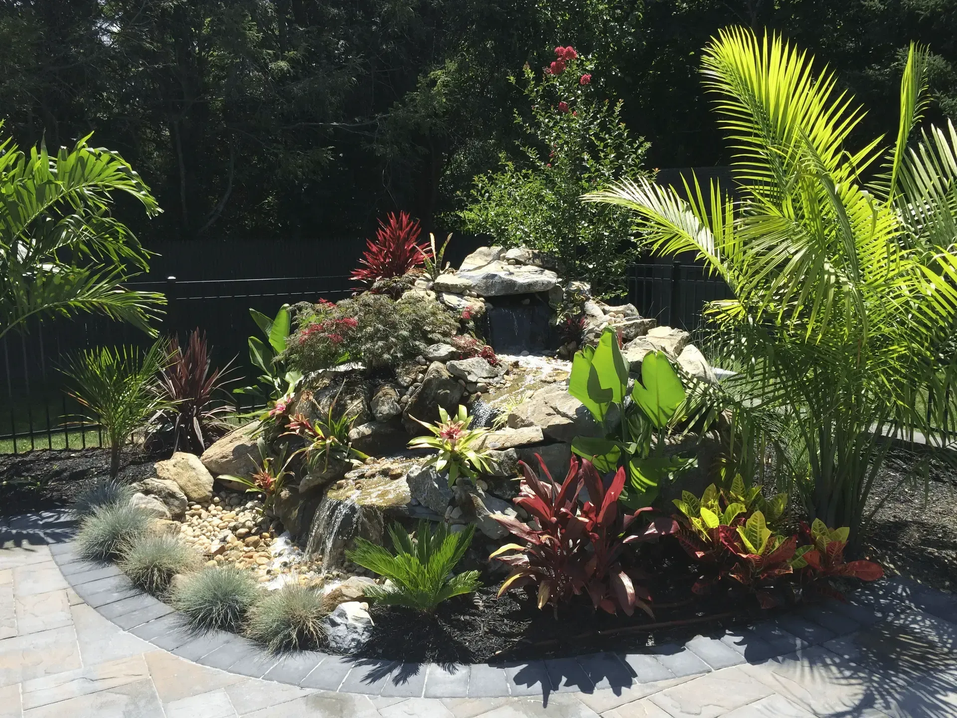 A decorative rock waterfall feature surrounded by lush tropical plants on a patio.