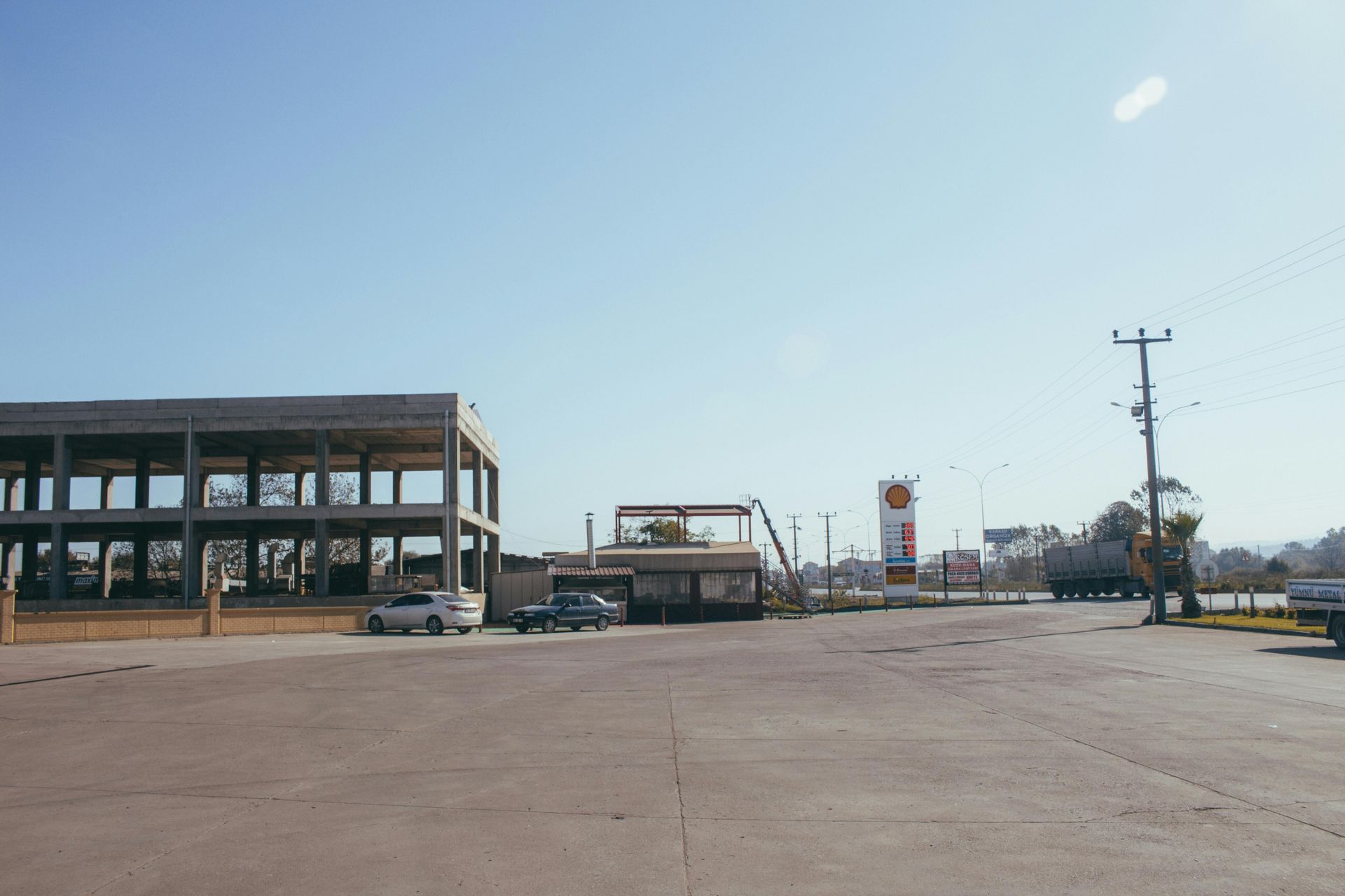 Open-air concrete structure and gas station on a clear, sunny day. Cars parked on the paved area.