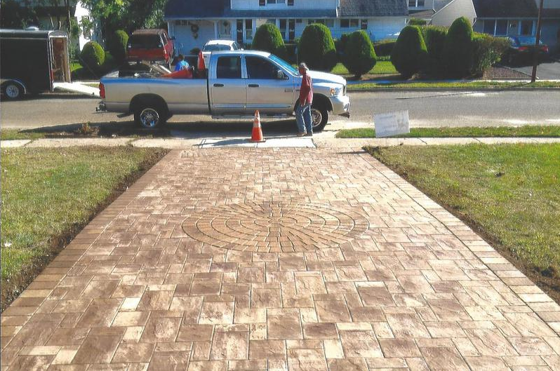 Brick driveway, worker near truck with materials; houses in background.