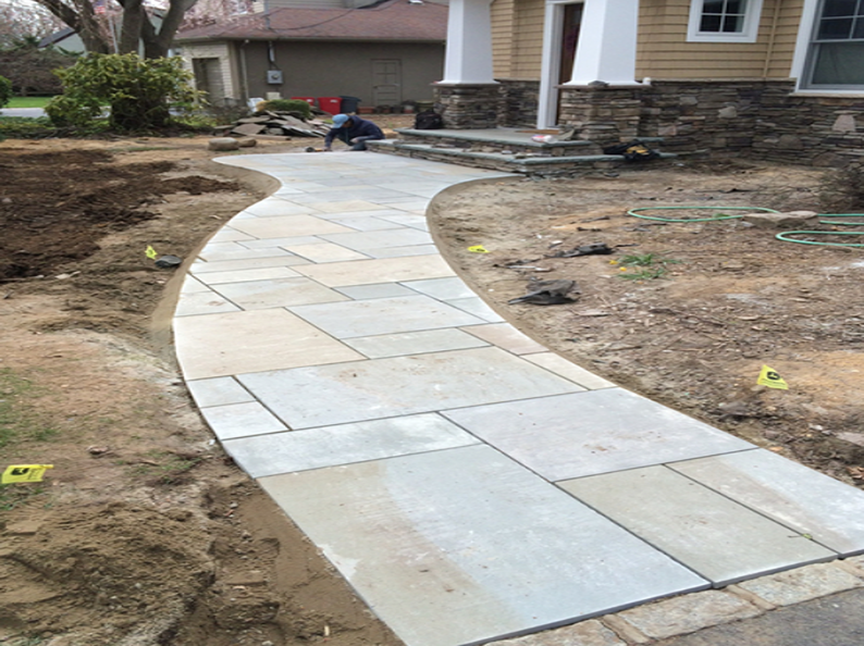 Stone walkway under construction leading to a house with beige siding and stone accents.