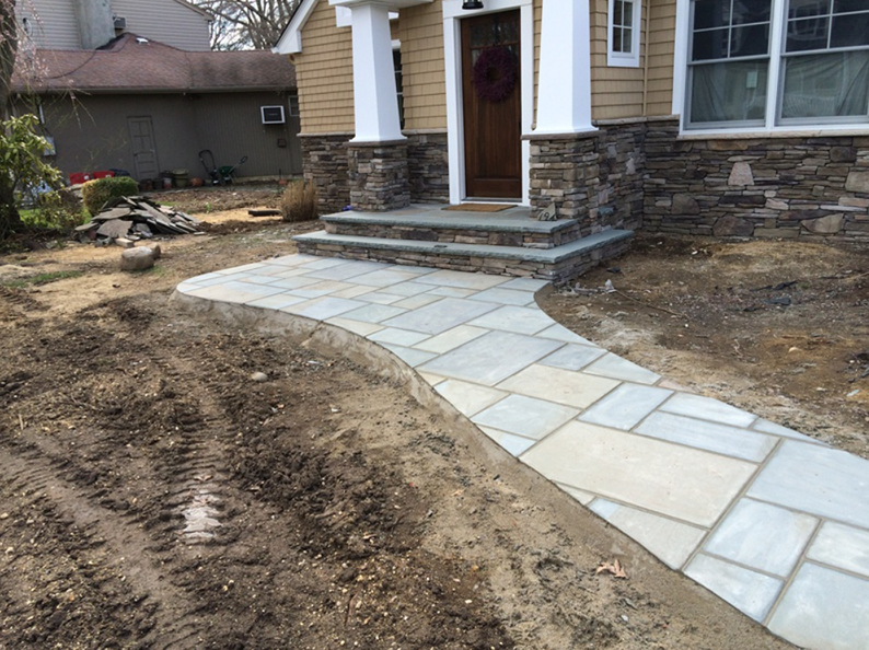 Stone walkway leading to a house's front door with stone steps and light yellow siding.
