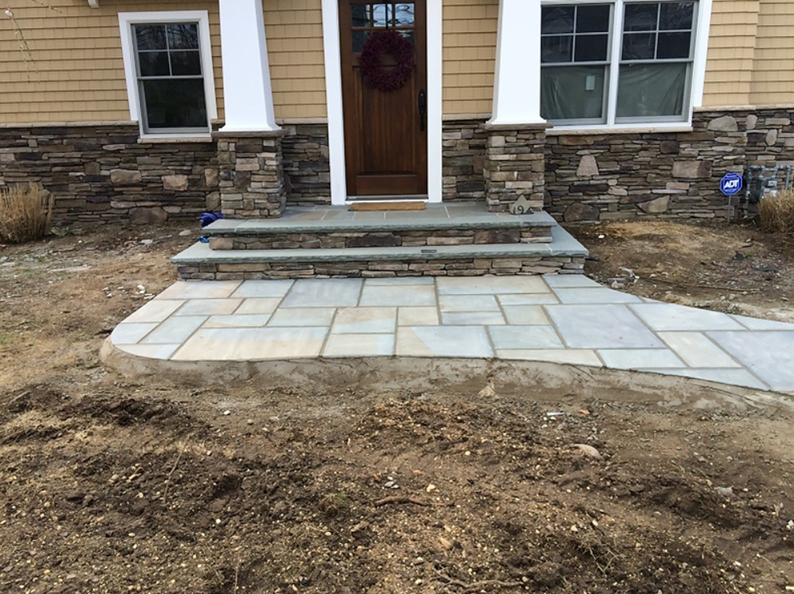 Stone steps and walkway leading to a front door with stone veneer and beige siding.