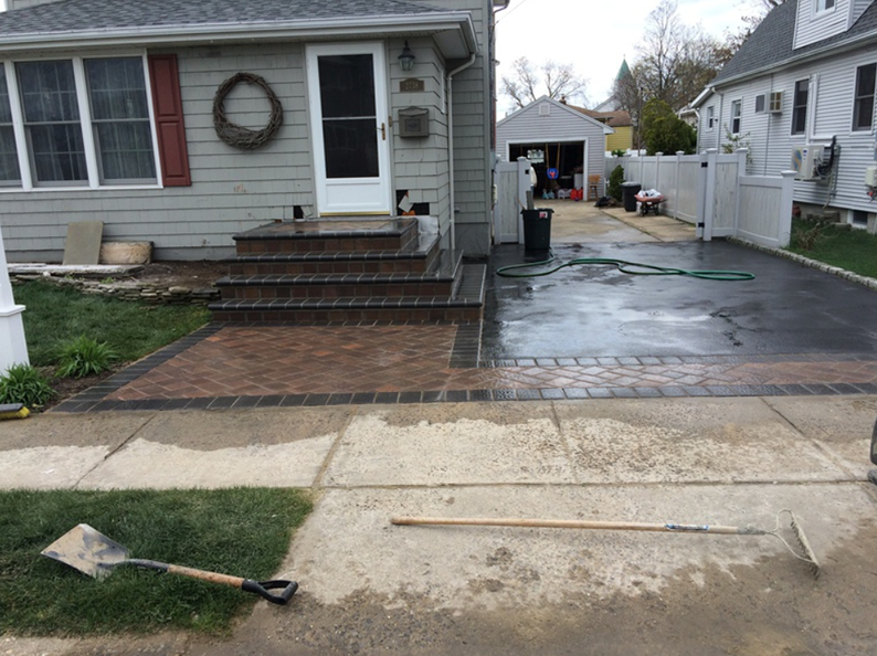 House entrance with brick steps and pathway, asphalt driveway. Shovel and tools on the ground.