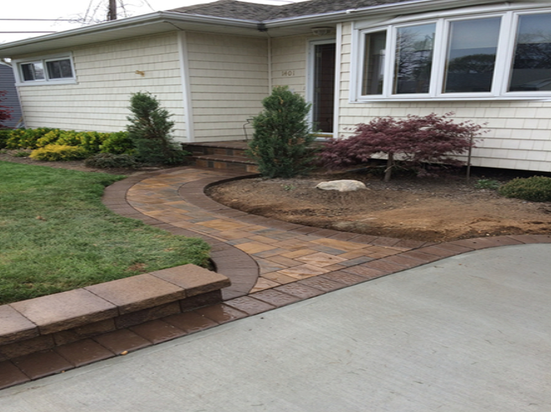 Brick pathway curves to a house entrance, a low wall, and landscaped beds.
