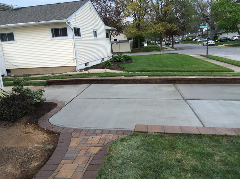 Concrete driveway with brick border leading to a house and street with grass.