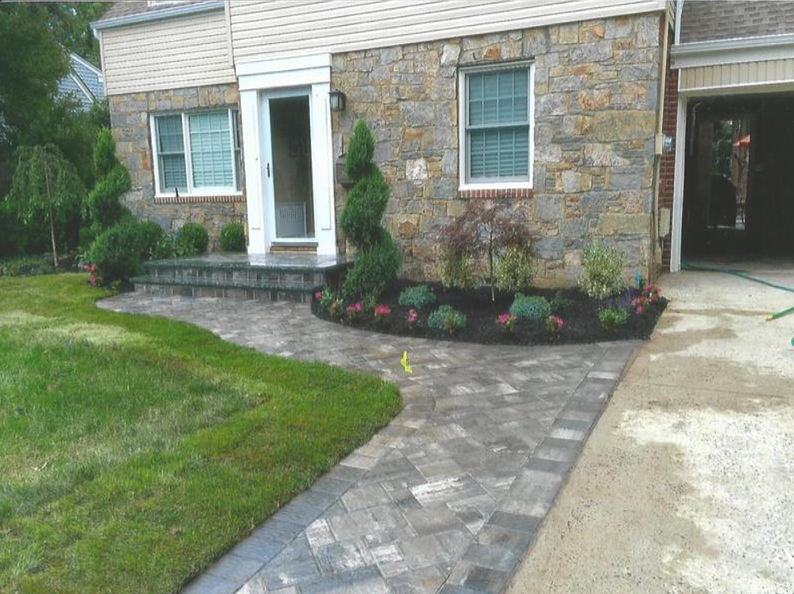 Stone house with paved walkway, flower beds, and a garage.