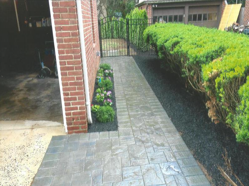 Brick house with a patterned walkway, a planted garden, and a black hedge.