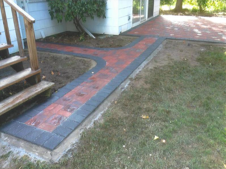 Brick patio and walkway with red and black pavers, leading to a house entrance.