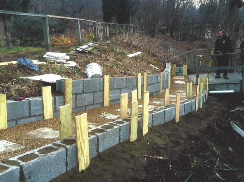 Construction of a curved retaining wall with cinder blocks and wooden supports on a hillside.