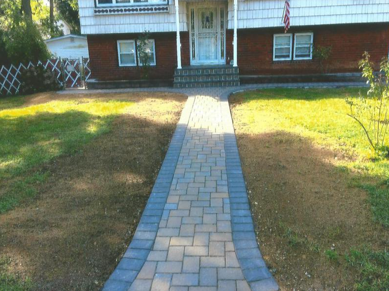Brick pathway leading to a house with a white facade, bordered by patchy brown and green lawn.