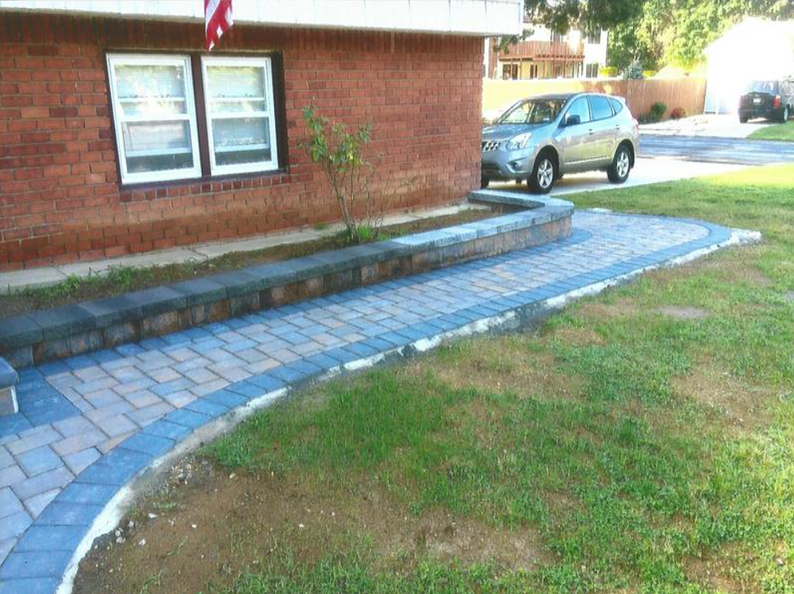 Brick building with a curved blue and tan brick path. A car is parked nearby on the driveway.