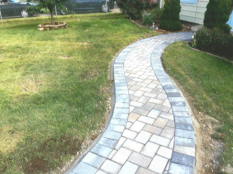 Brick walkway curves through a grassy lawn, leading toward a house.