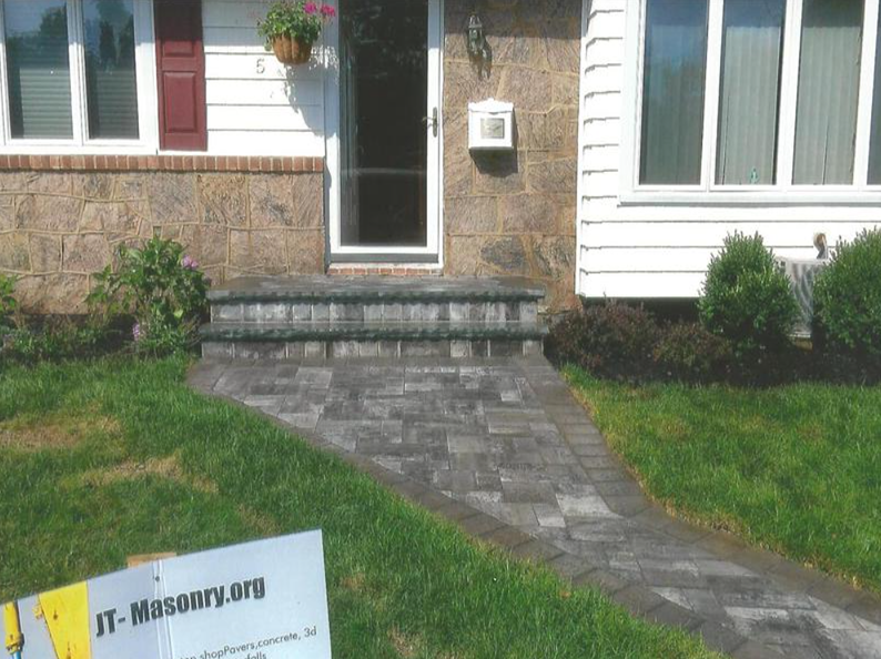 Stone pathway leads to a house with a front door and small steps; grass surrounds.