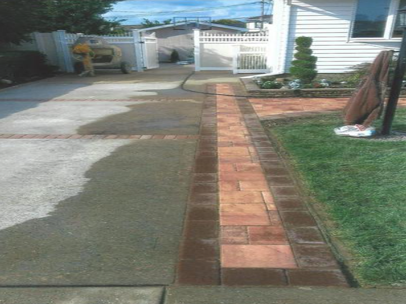 Driveway with brick-bordered walkway; a person works near a house with a white fence and garage.