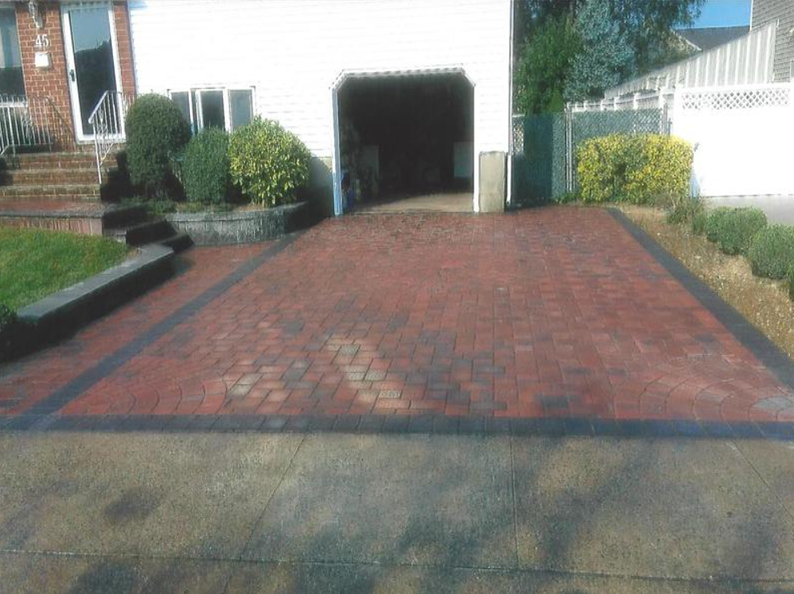 Brick driveway leading to a garage. Red bricks with black border, some wet spots, residential setting.