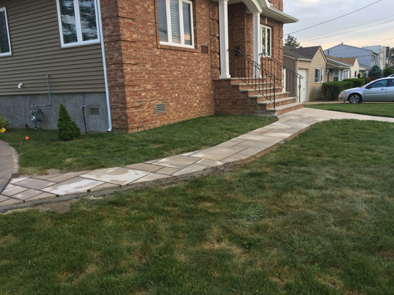 Brick house with stone walkway leading to front steps, surrounded by green lawn.