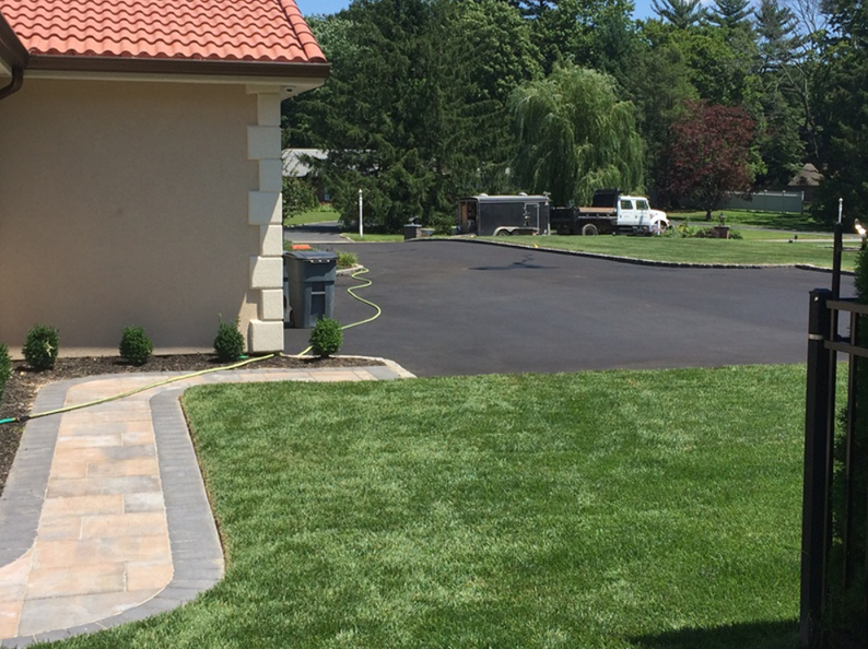 A tan-colored house with a red tiled roof next to a fresh asphalt driveway and green lawn.
