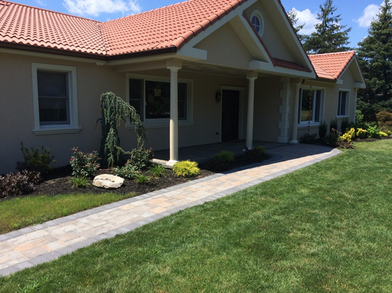 Beige house with orange tile roof, pathway, and green lawn.