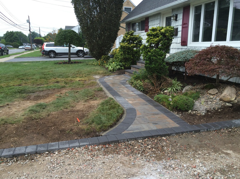 Paver walkway leading to a house, with landscaped beds, gravel and lawn.