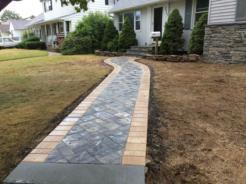Brick pathway leading to a house with brown trim, surrounded by grass.