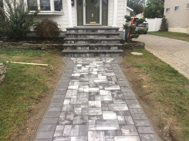 Brick pathway leading to gray stone steps in front of a white house.