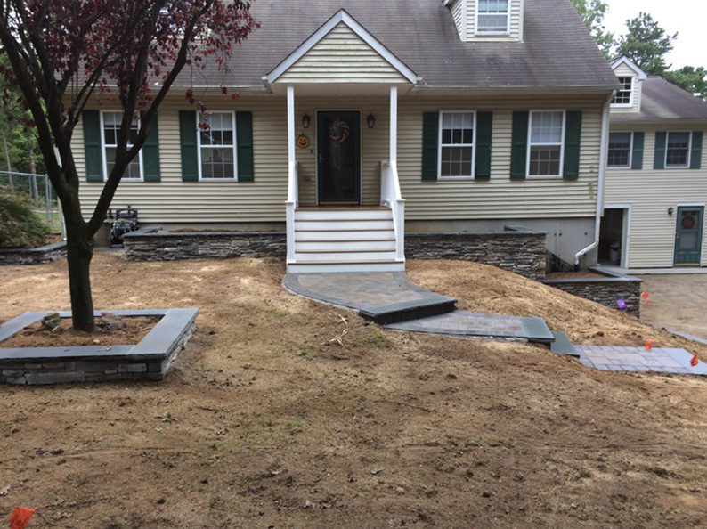 Beige house with new stone retaining walls and pathway in a yard of fresh dirt.