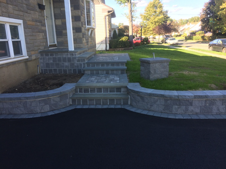 Gray brick steps and retaining wall in front of a house, on a sunny day.