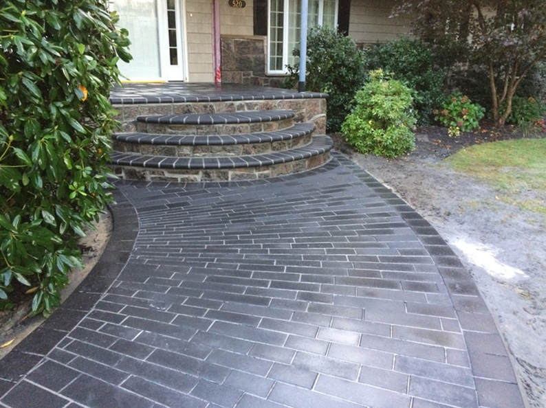 Brick walkway and steps leading to a house entrance. Dark gray bricks with a curved border.