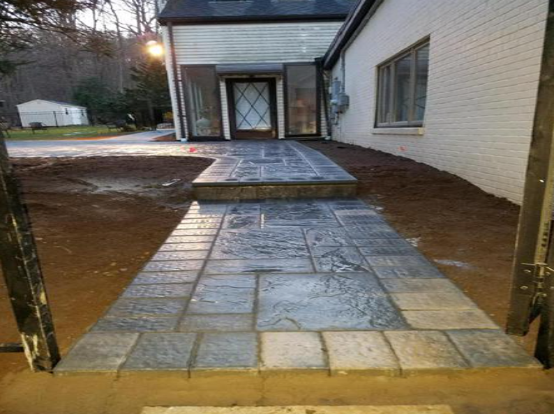 Pathway leading to a house with steps, grey stamped concrete, surrounded by dirt.