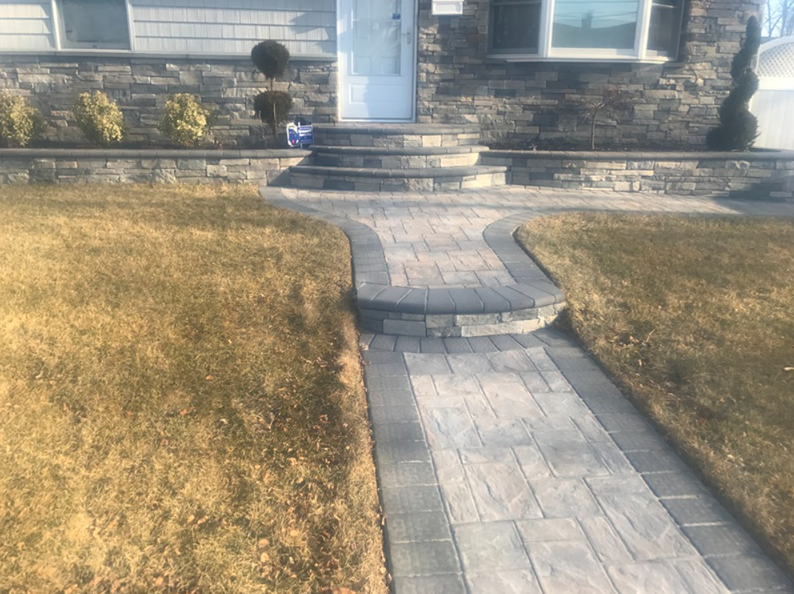 Stone walkway leading to a house with stone facade and steps, flanked by brown grass.