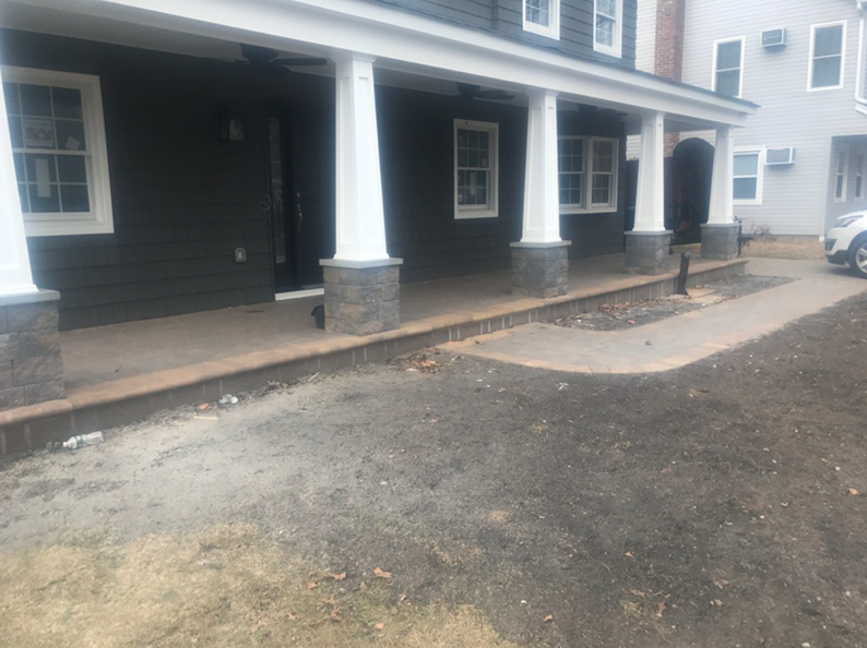 A dark house with a white-columned porch and a stone path leading to it.