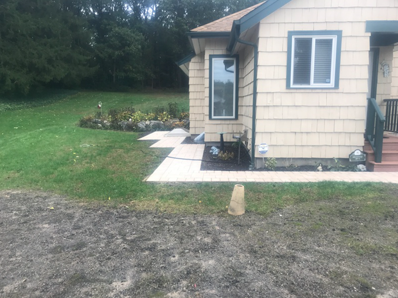 Beige house with pathway, garden, and grassy lawn; overcast day.