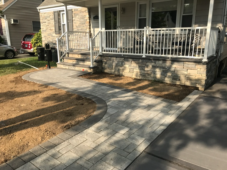 Stone walkway curving towards a house with stone facade and white porch railing.