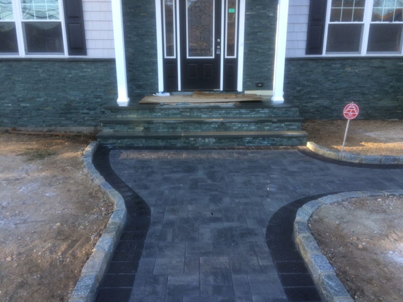 Brick pathway leading to a house's front steps and door. Grey brick, black border, with green/black brick on exterior.
