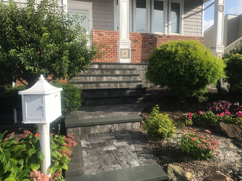 White mailbox, brick steps leading to house with green shrubbery and flower beds.