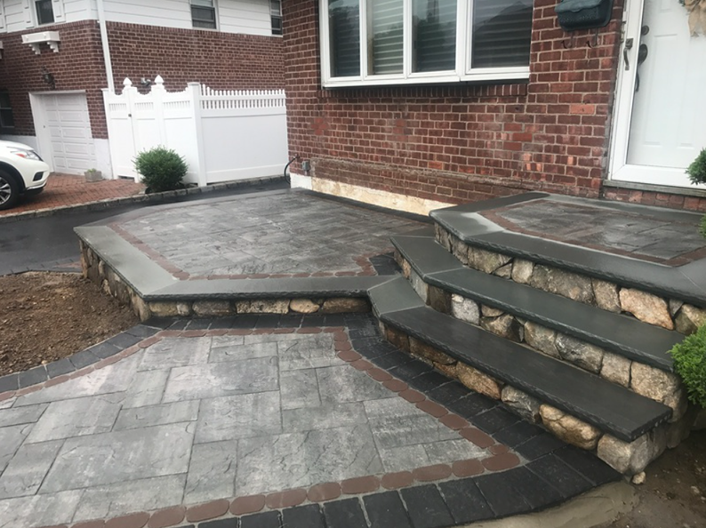 Brick home entrance with stone steps and patio with gray and brown pavers.
