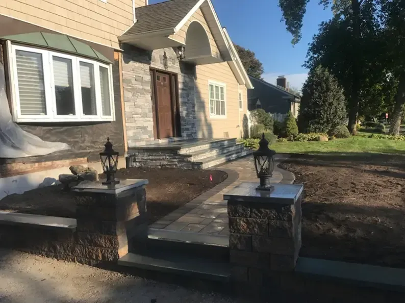 House with stone steps, walkway, and lampposts, on a sunny day.