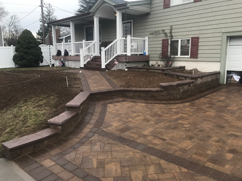 Brick walkway and retaining wall lead to a light green house with a porch and front steps.