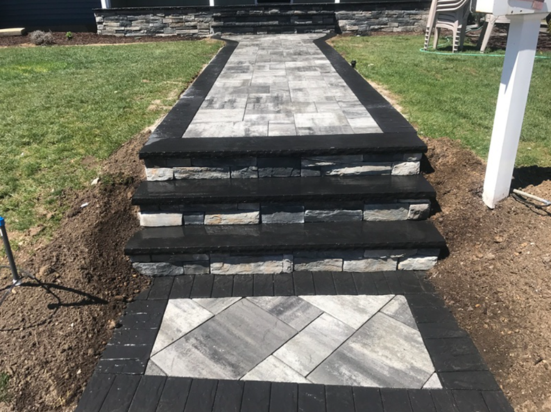Stone walkway with steps leading to a house entrance. Dark border surrounds grey stone path.