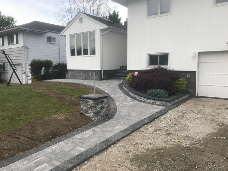 Paved walkway leading to a white house with a grey stone border and small garden.