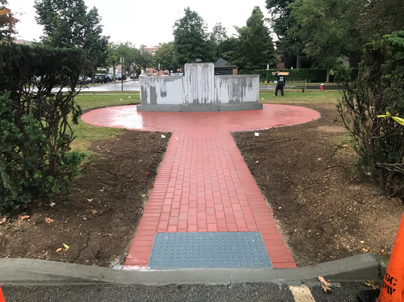 Red brick path leads to a monument in a park; work in progress with construction cones and dirt.