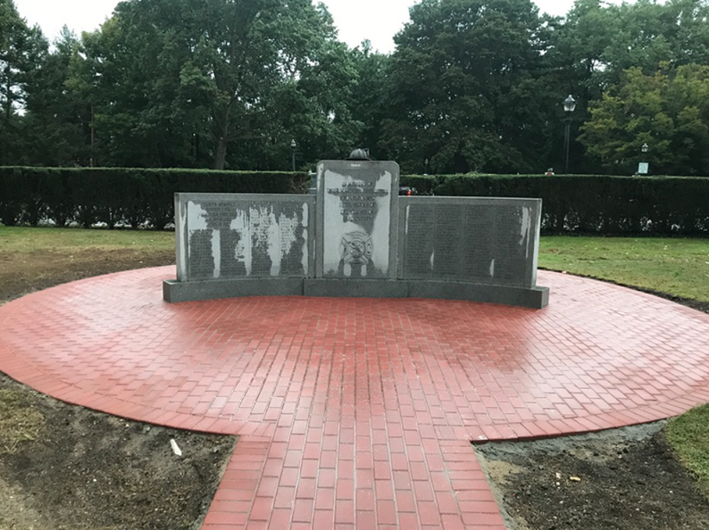 Memorial with names on it, surrounded by red brick, in a park setting.