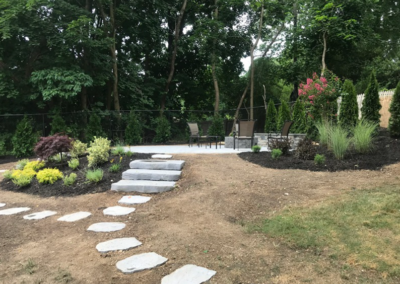 Stone pathway leads to a patio with seating, surrounded by landscaping.