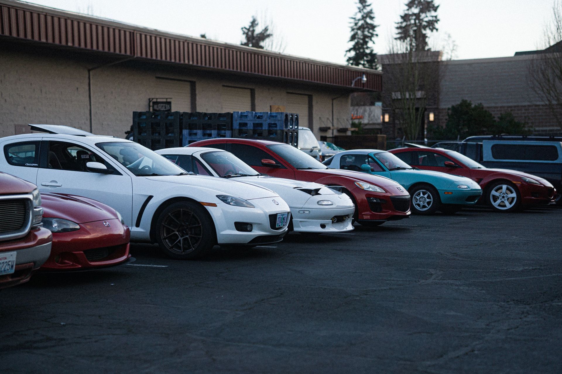 Row of parked sports cars in white, red, and blue outside a building at dusk