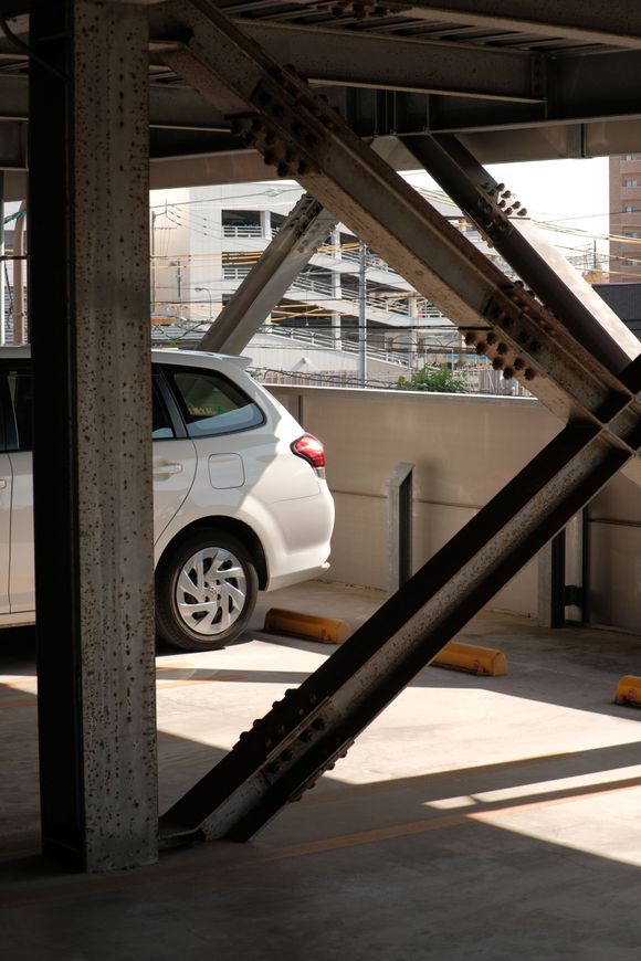 White car parked under a concrete structure with metal beams and city buildings in the background