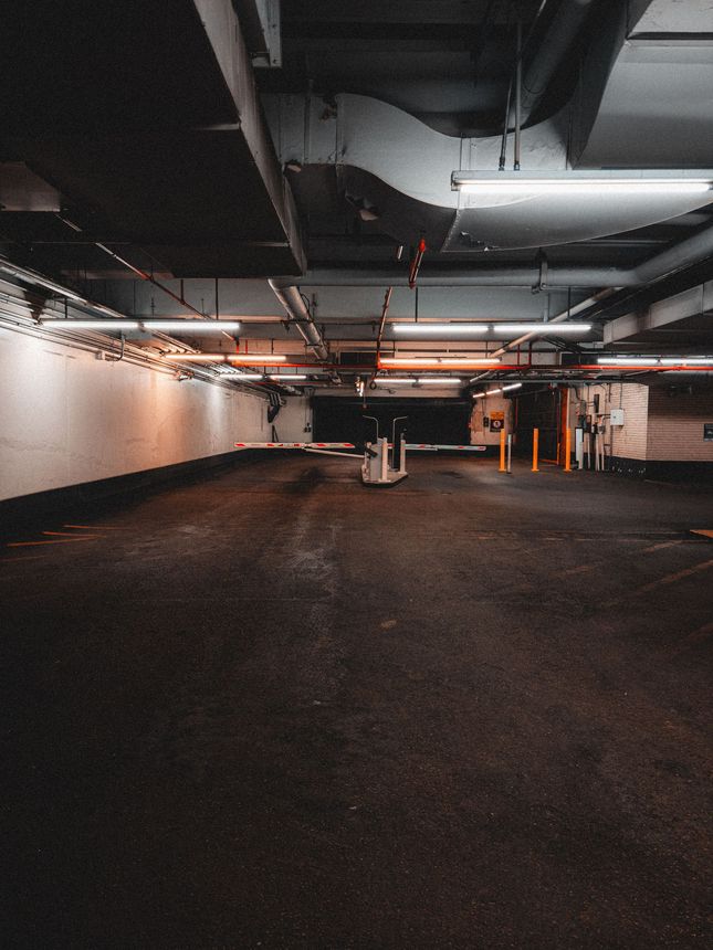 White car parked under a concrete structure with metal beams and city buildings in the background