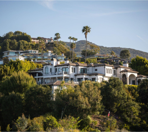 A large white house sits on top of a hill surrounded by trees